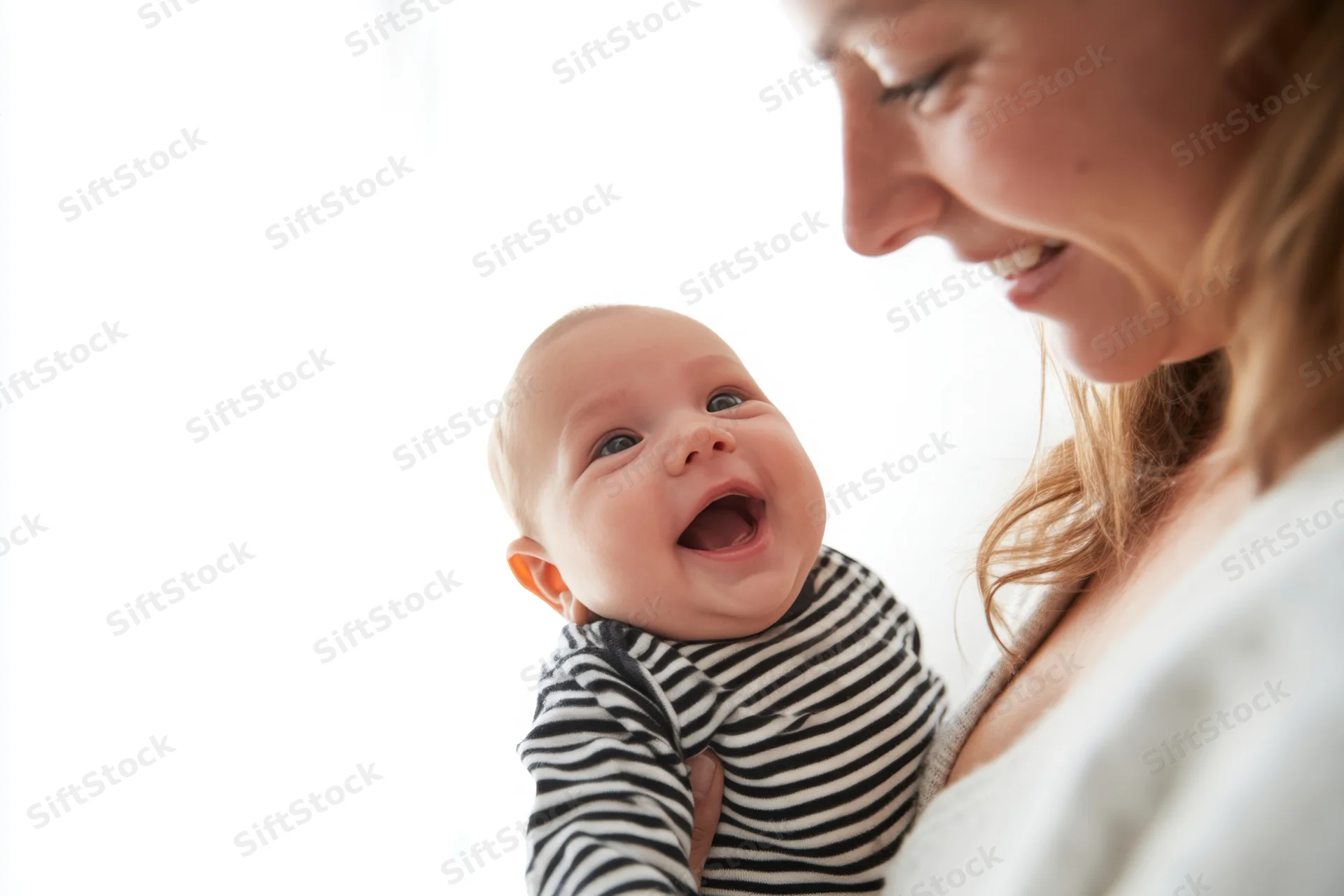Mother holding smiling baby in striped onesie indoors