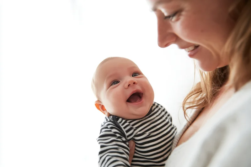 Mother holding smiling baby in striped onesie indoors