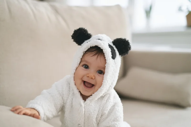 Baby in panda costume smiling on beige couch