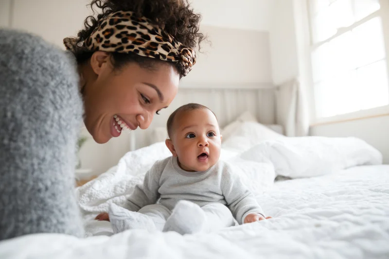 Mother smiling at baby sitting on bed in bedroom
