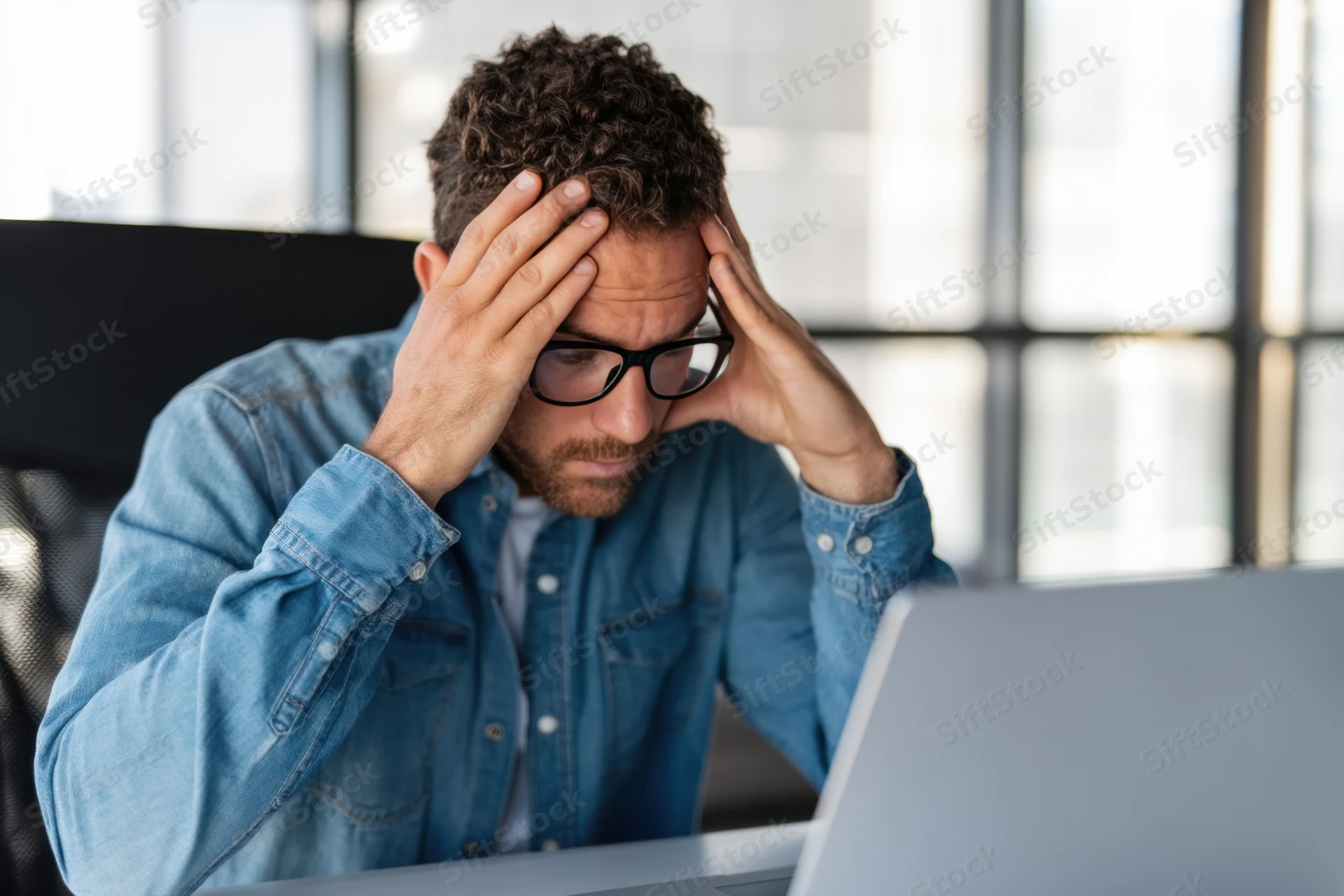 Man with hands on head looking at laptop in modern office