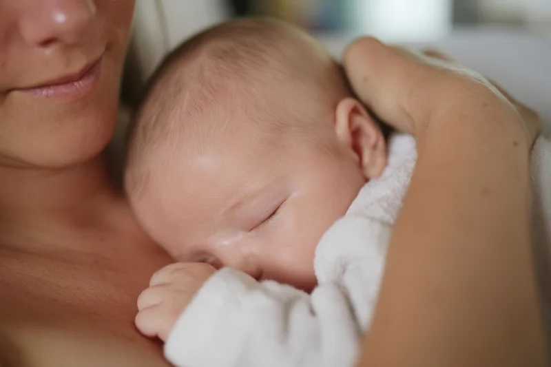 Mother cradling sleeping newborn close to her chest wrapped in white towel