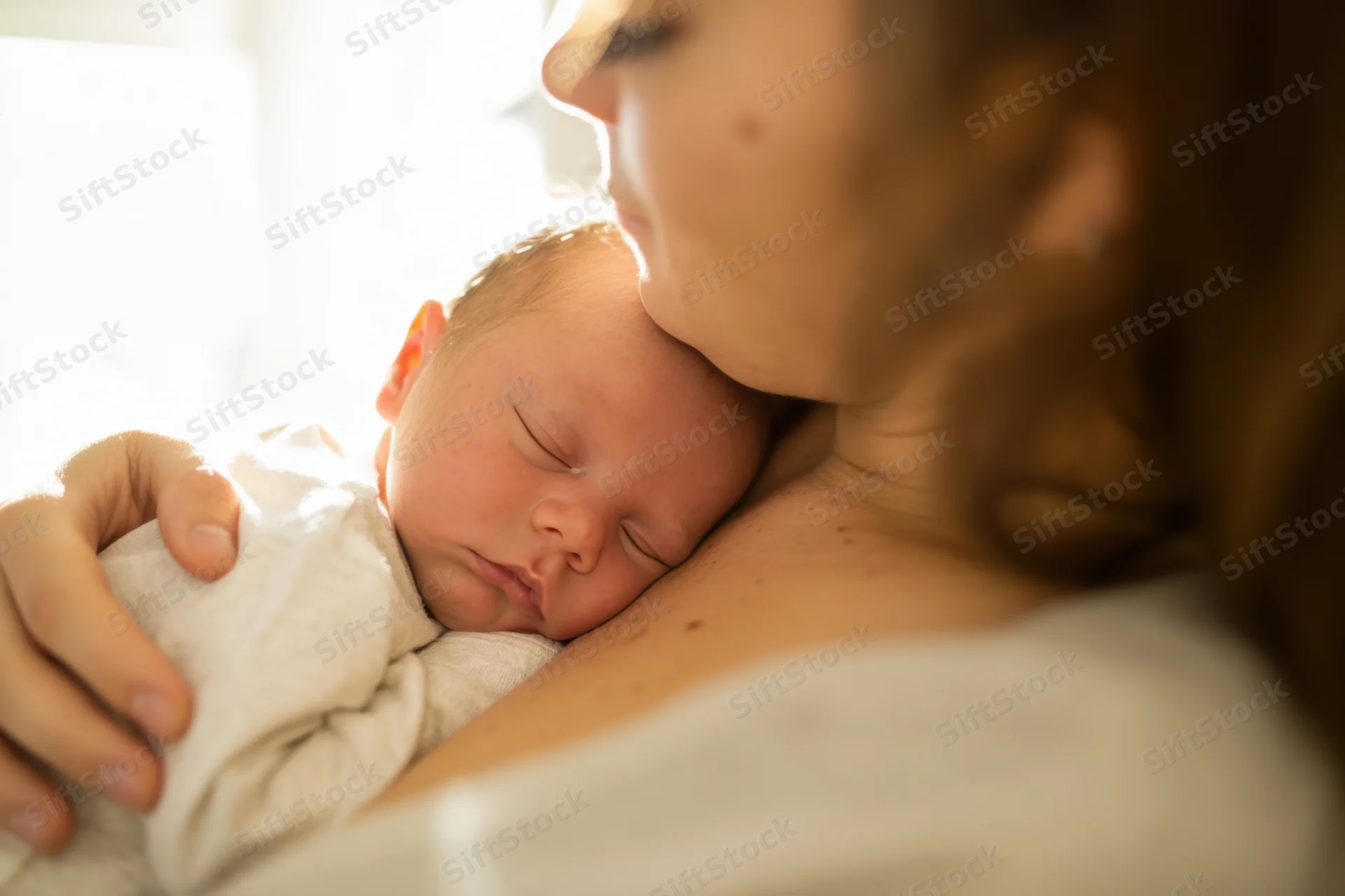 Mother cradling sleeping newborn close to her chest indoors
