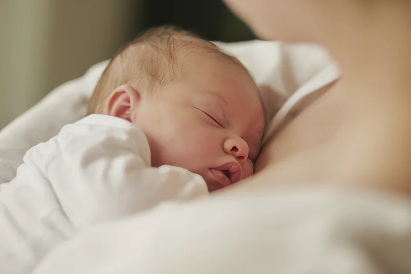 Newborn baby sleeping on mother's chest wrapped in white blanket