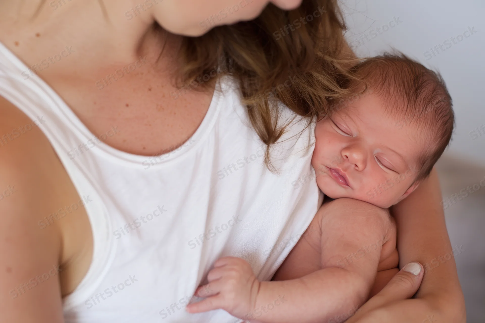 Mother cradling sleeping newborn close to her chest indoors