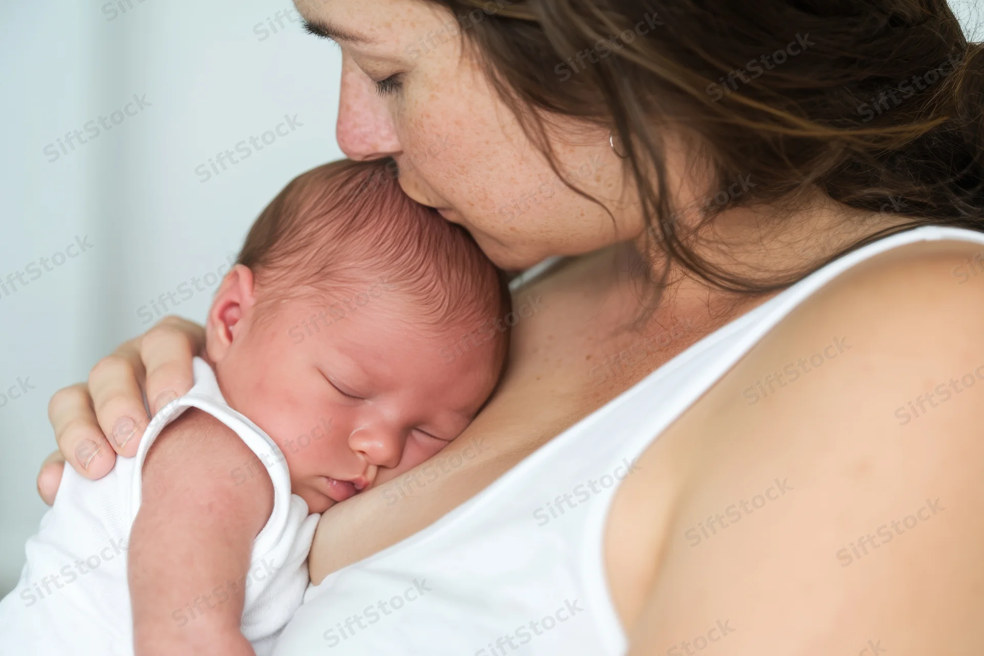 Mother cradling sleeping newborn close to her chest indoors