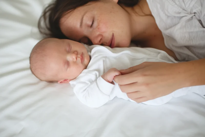Mother sleeping beside her newborn baby on a white bed