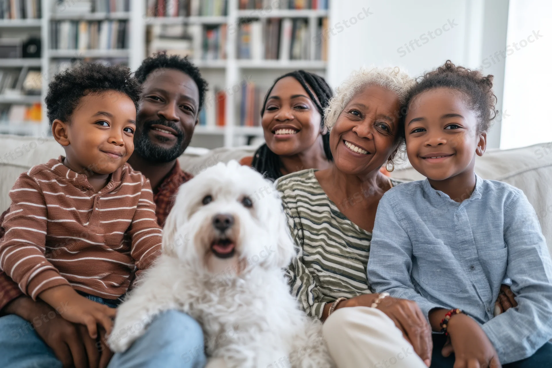 Multi-generational family smiling together on a couch with a white fluffy dog in a living room with bookshelves