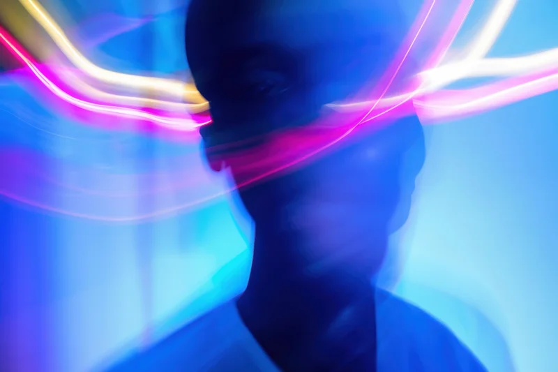 Motion-blurred portrait of a man in neon light trails against a blue background