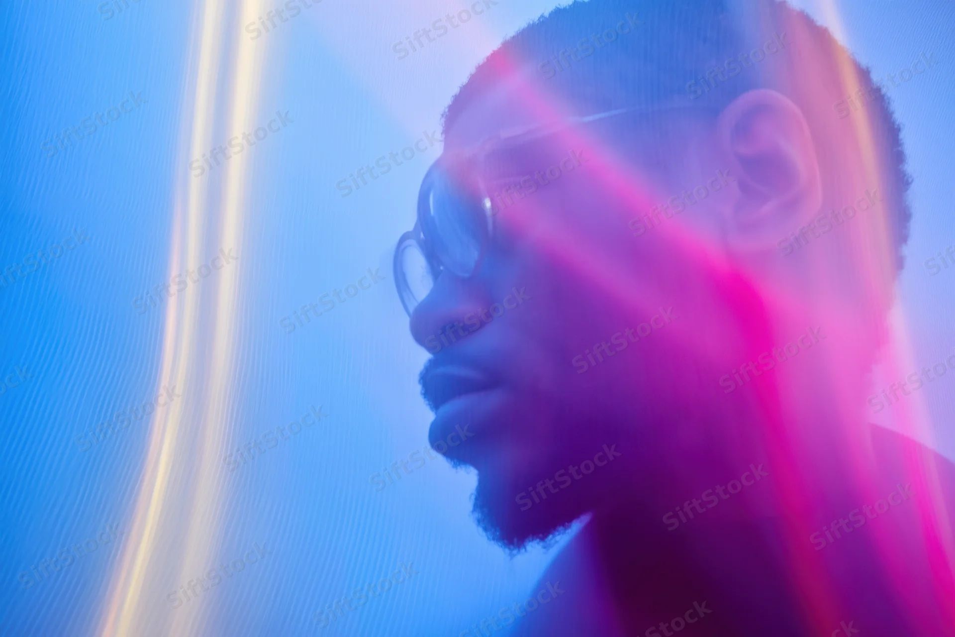 Man in side profile with glasses and beard under neon blue and pink light, motion blurred portrait