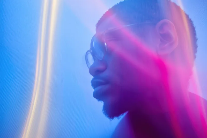 Man in side profile with glasses and beard under neon blue and pink light, motion blurred portrait