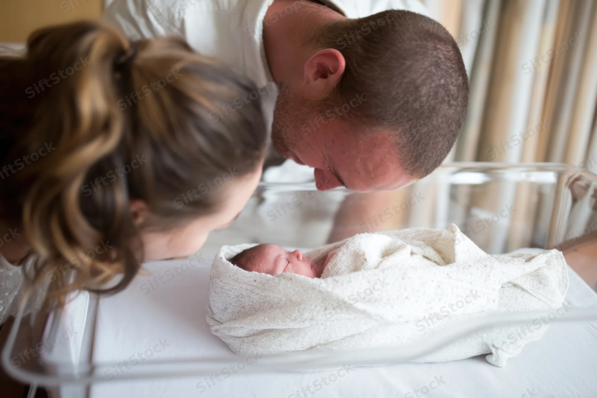 New parents leaning over their swaddled newborn in a hospital bassinet