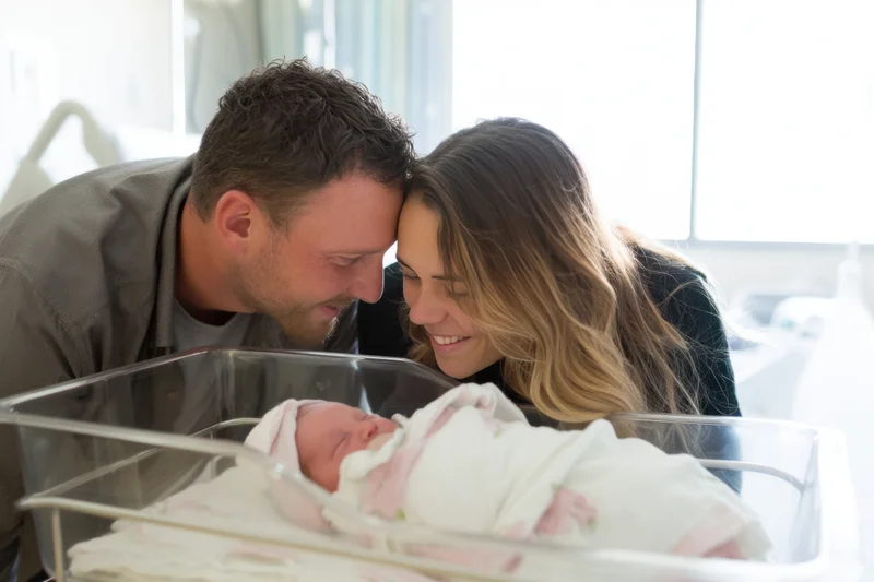Parents leaning over newborn in hospital bassinet, touching foreheads, smiling