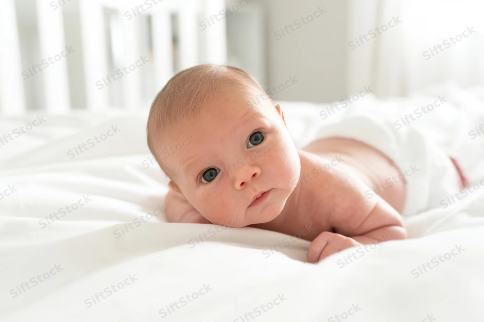 Newborn baby lying on stomach on white blanket in crib