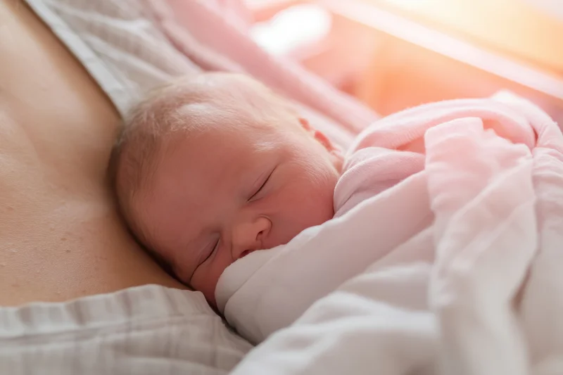 Newborn baby sleeping peacefully on mother's chest wrapped in soft pink blanket