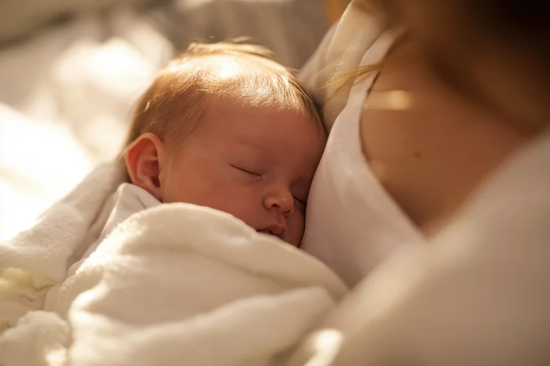 Newborn baby sleeping peacefully in caregiver's arms wrapped in white blanket
