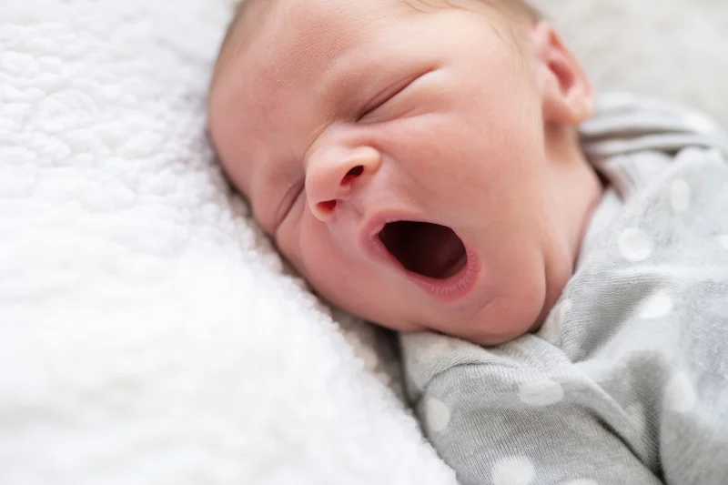 Newborn baby yawning while resting on a soft white plush blanket