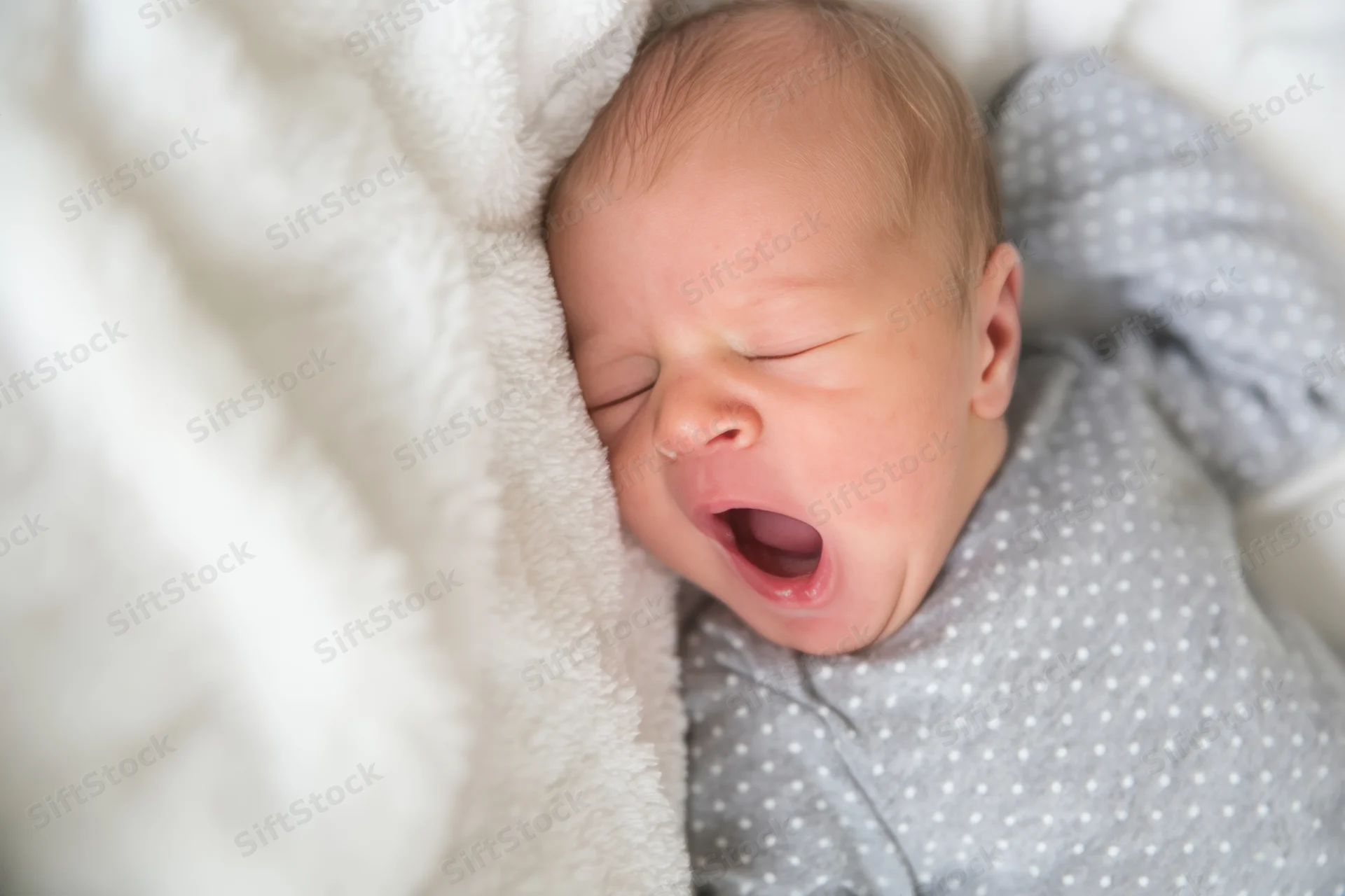 Newborn baby yawning while resting on a soft white plush blanket