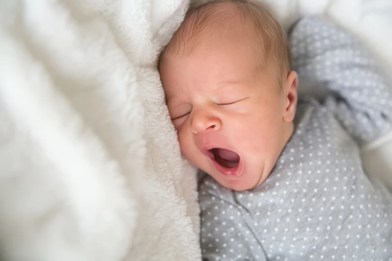 Newborn baby yawning while resting on a soft white plush blanket