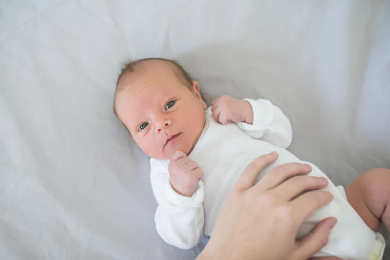 Newborn baby lying on soft gray surface with hand gently touching its body