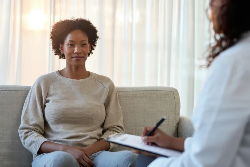 Woman sitting on sofa smiling during therapy session with clinician