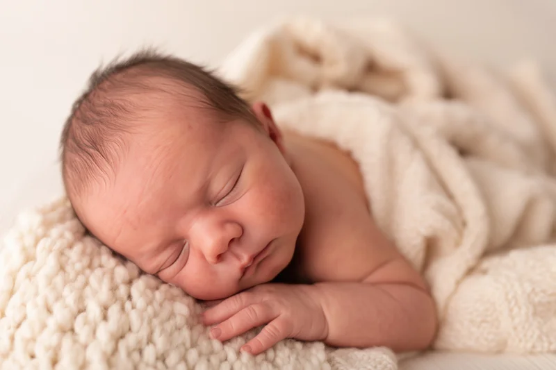Newborn sleeping peacefully on a cream knitted blanket in a studio portrait