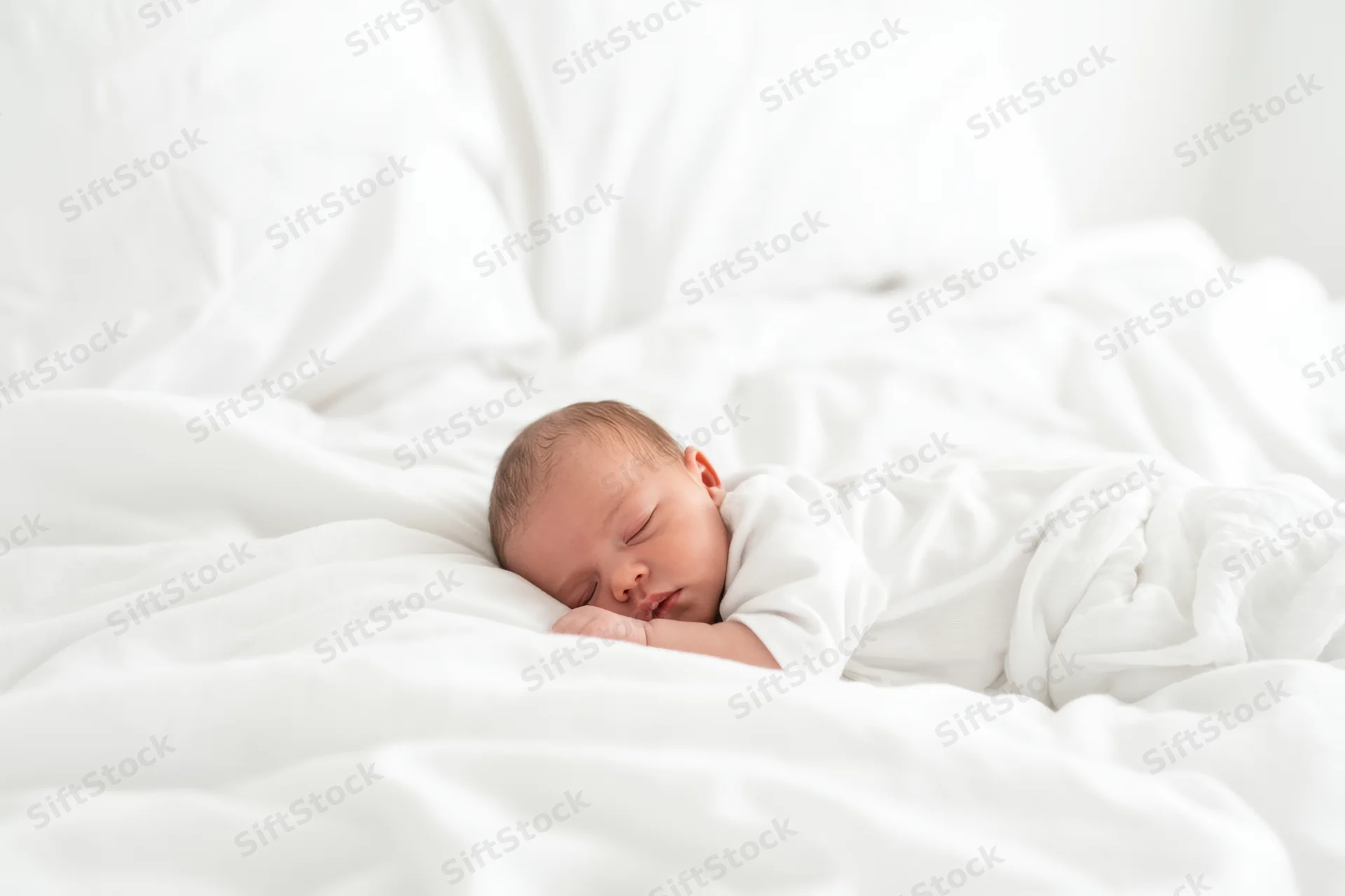 Newborn baby sleeping peacefully on a white bed wrapped in white fabric