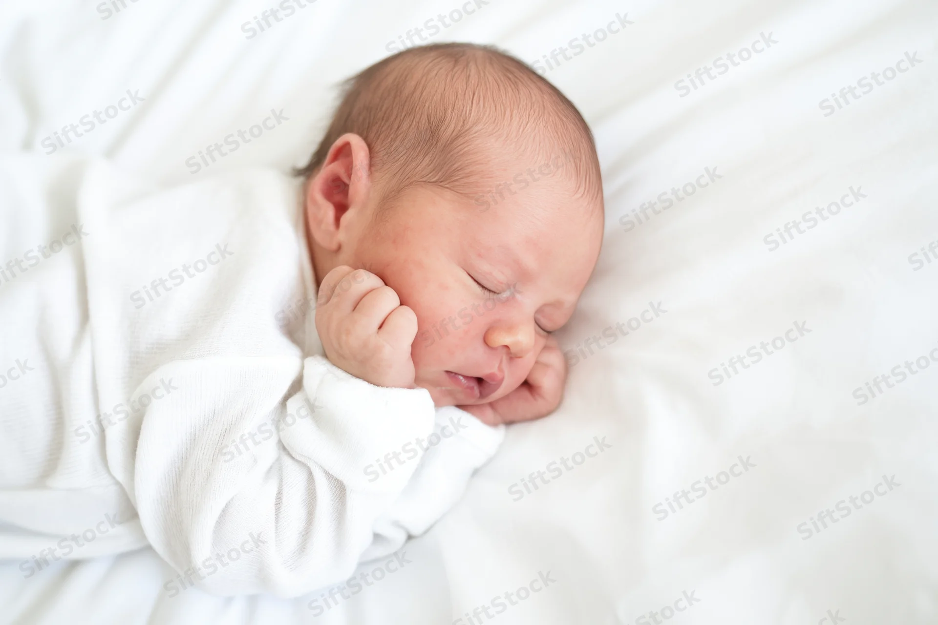 Newborn baby sleeping peacefully on white blanket in crib