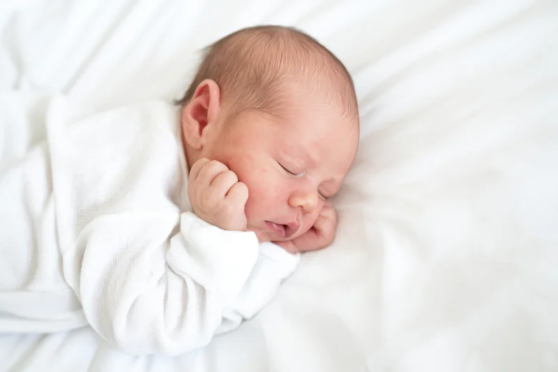 Newborn baby sleeping peacefully on white blanket in crib