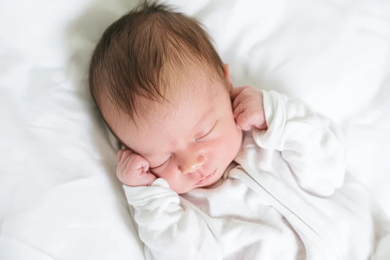 Newborn baby sleeping peacefully on a white bed with hands near face