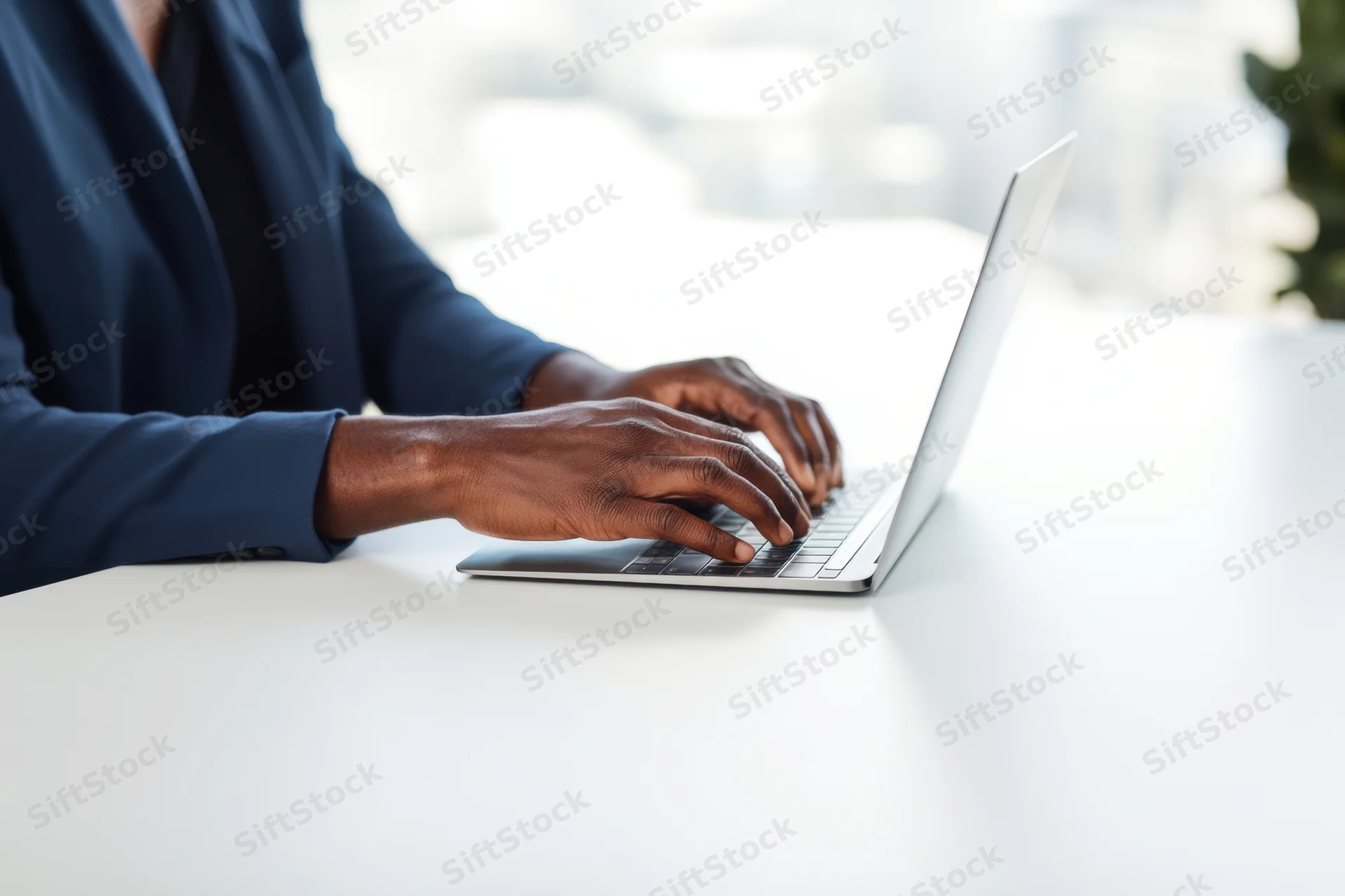 Woman in dark blue blazer typing on silver laptop at white desk