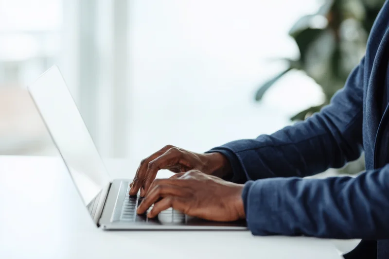 Man in dark blue blazer typing on slim silver laptop at white desk