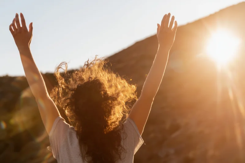 Woman with arms raised facing sun on hillside
