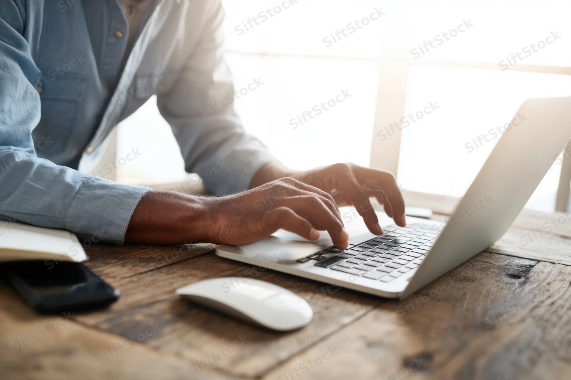 Man typing on silver laptop at rustic wooden desk
