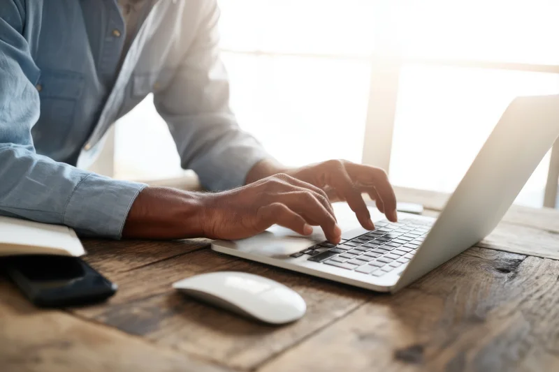 Man typing on silver laptop at rustic wooden desk