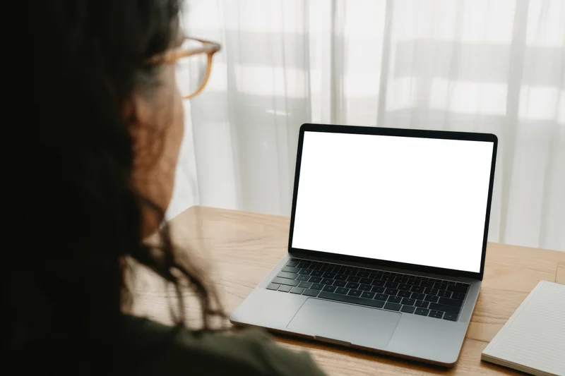 Woman viewing blank laptop screen at wooden desk by window