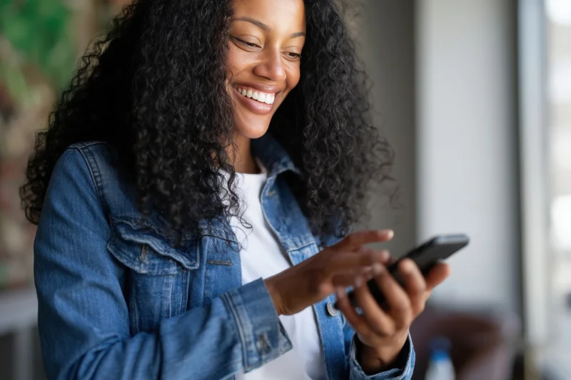 Smiling woman using smartphone while wearing denim jacket indoors