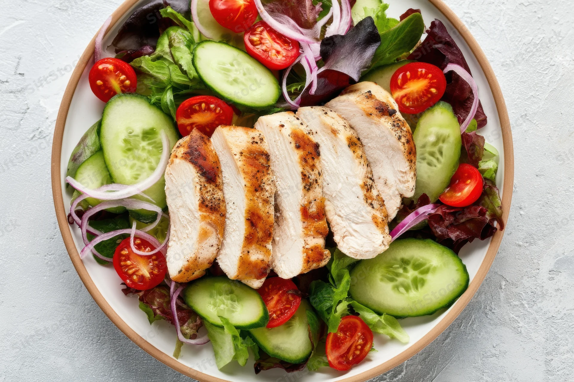 Grilled chicken slices on a mixed salad with tomatoes cucumbers and red onions on a plate