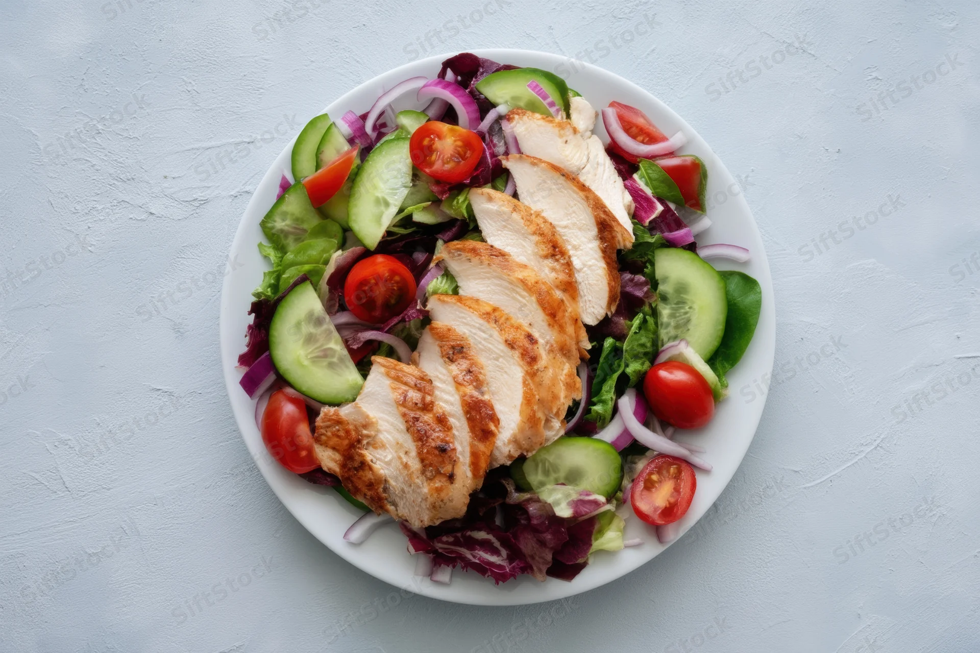 Grilled chicken slices on a mixed vegetable salad served on a white plate