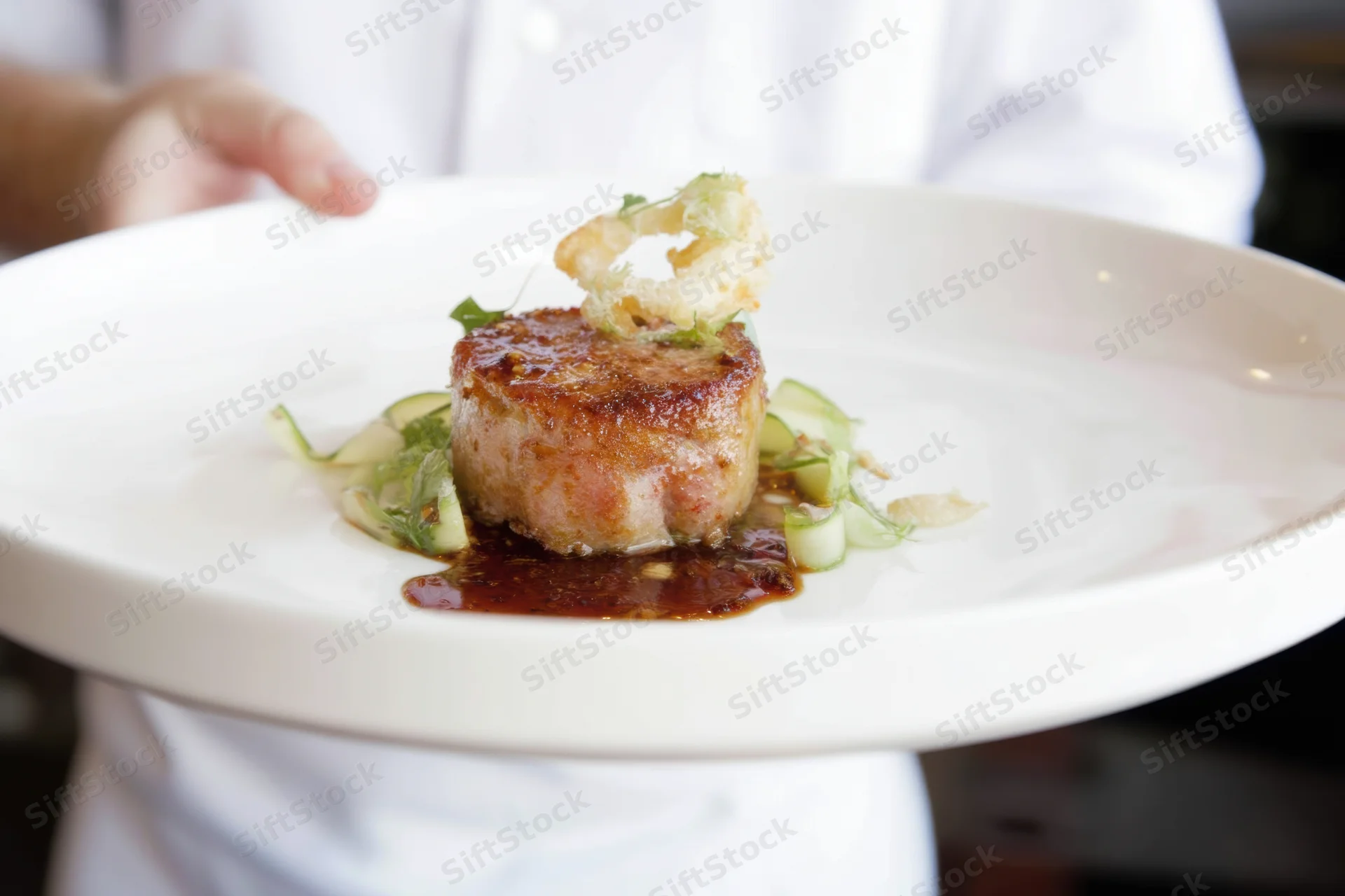 Chef holding a white plate with a seared meat medallion garnished with herbs and sauce