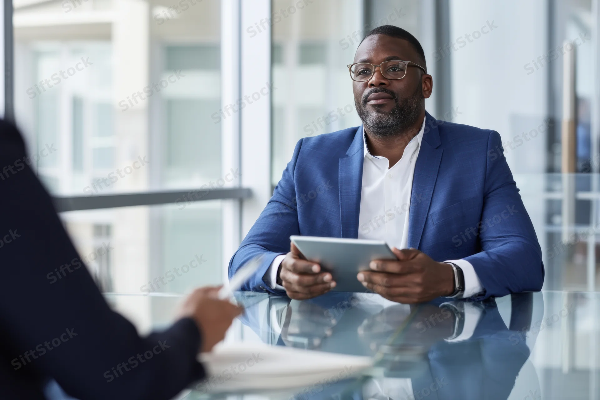 Businessman in blue suit holding tablet during meeting at glass desk in office