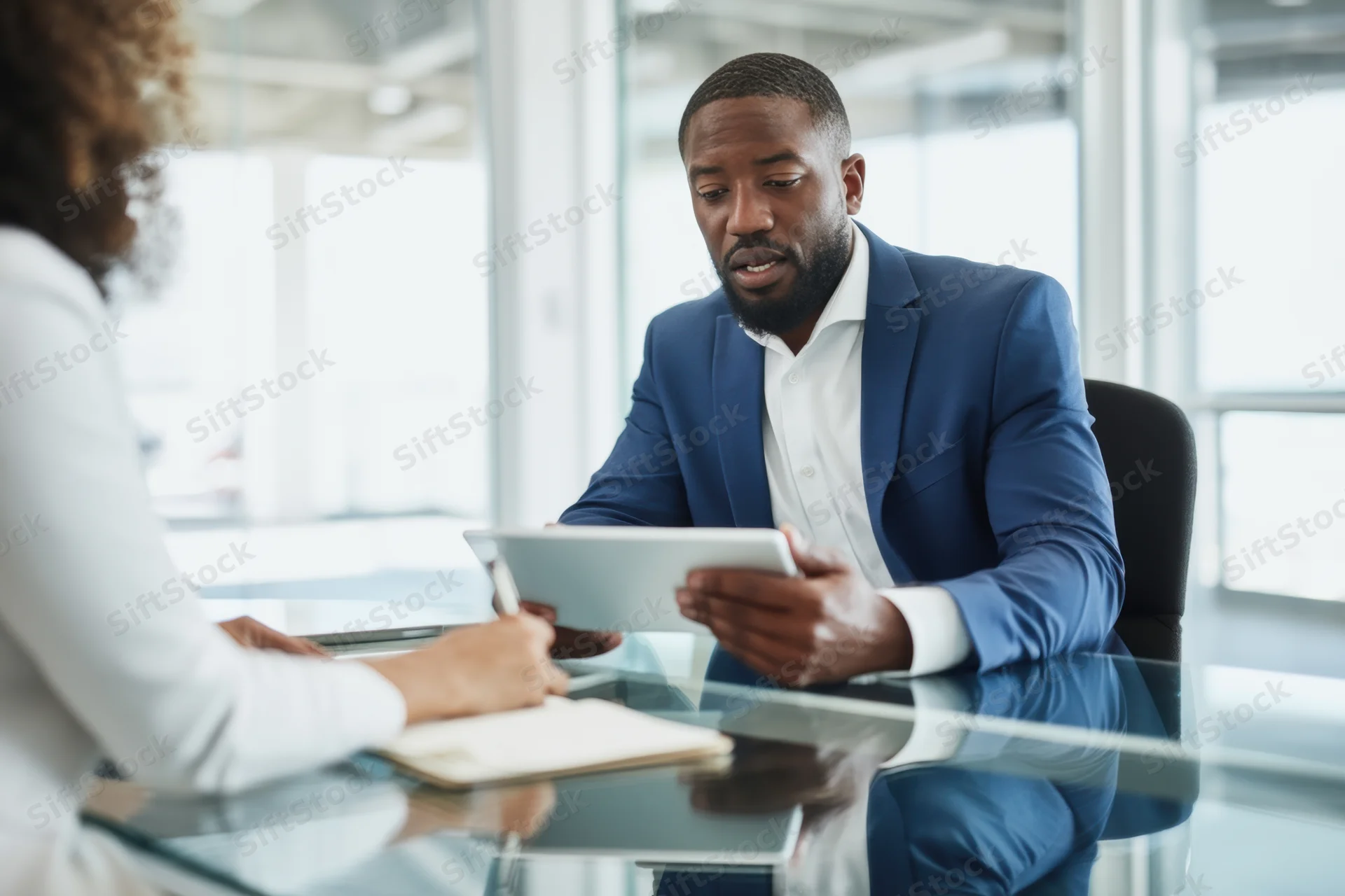 Businessman in blue suit discussing with woman at glass desk in office