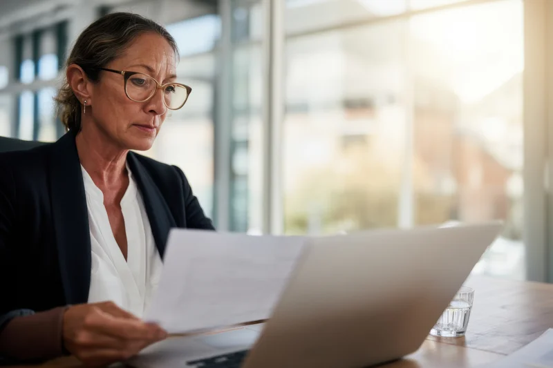 Woman reading document at laptop in modern office