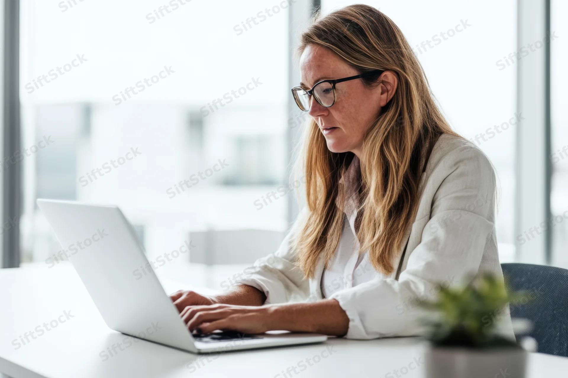 Woman typing on laptop at office desk near window