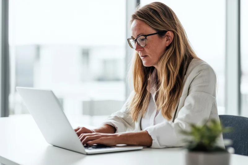 Woman typing on laptop at office desk near window