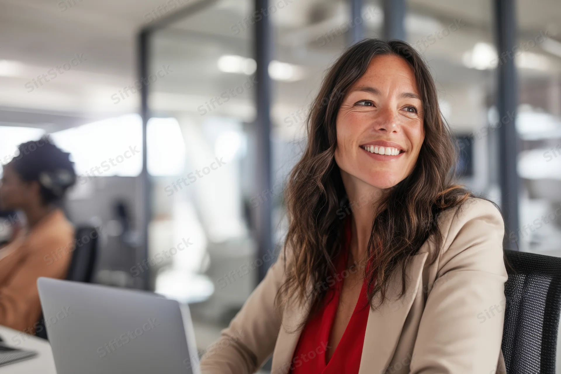 Woman smiling at camera while sitting at desk with laptop in modern office