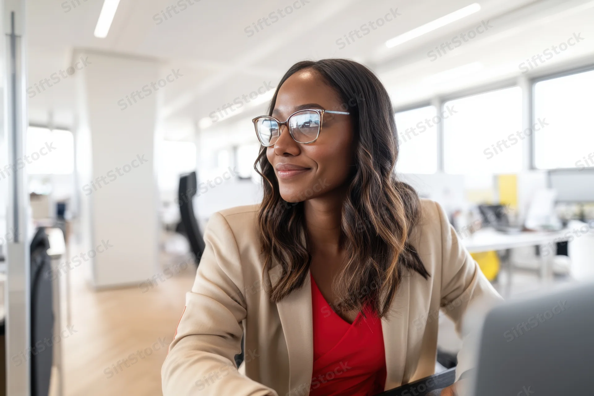 Woman in beige jacket smiling while working at computer in modern office