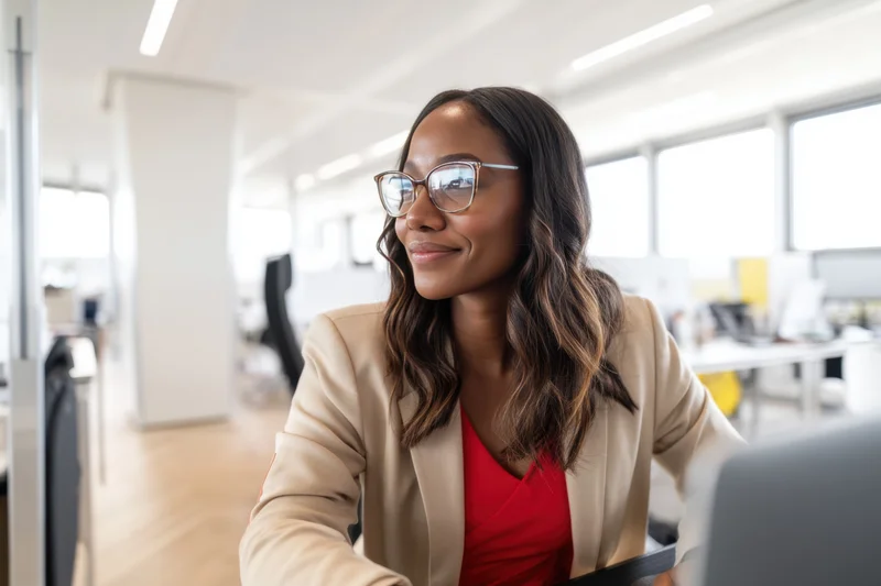 Woman in beige jacket smiling while working at computer in modern office