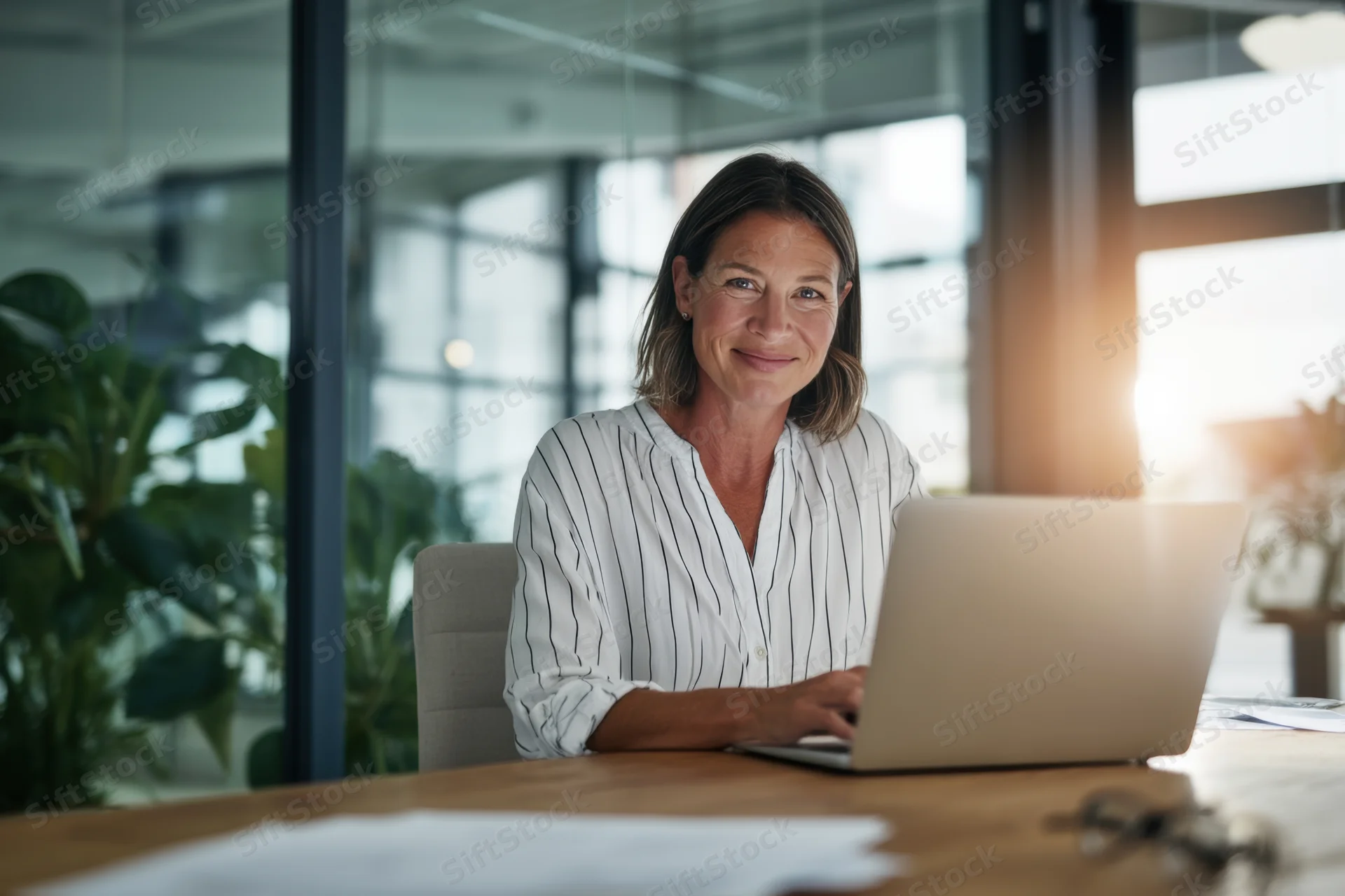 Woman smiling at camera while working on laptop at office desk