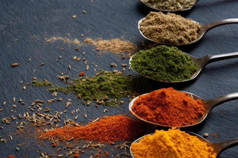 Row of spoons filled with colorful spices and herbs arranged on dark slate surface